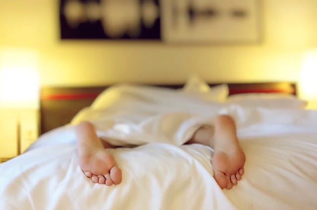 una persona tumbada en la cama tapada con una sábana blanca
