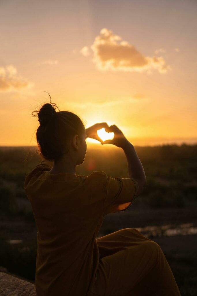 mujer joven hace forma corazón con las manos al aterdecer